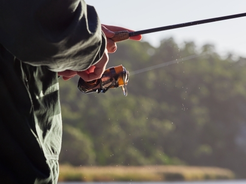 Close up of Man winding Fishing Reel while Holding a Rod