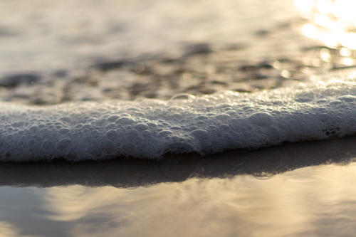 Close up of ocean water with sea foam washing up on wet sand - Australian Stock Image