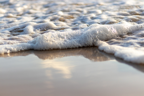 Close up of ocean water with sea foam washing up on wet sand - Australian Stock Image