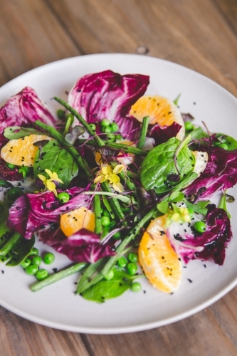 Low angle close up of naturally lit, fresh, colourful vegetable salad on timber table - Australian Stock Image