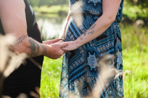 Close up of pregnant couple holding hands - Australian Stock Image
