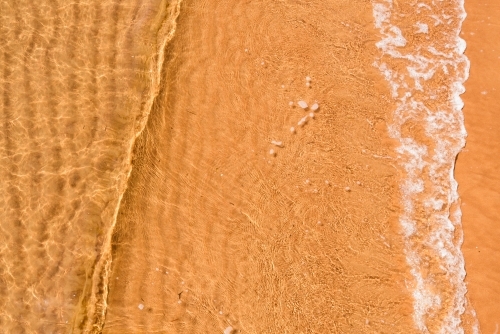 Close up of small wave over rippled sand