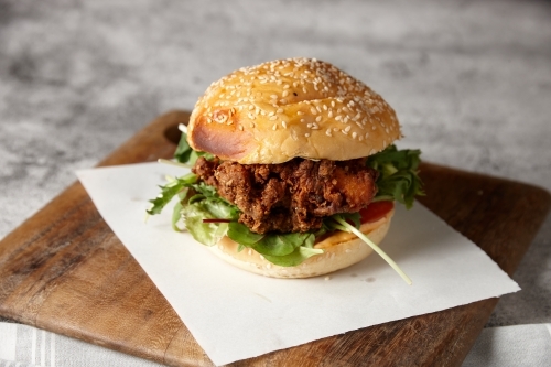 Close up of tasty fried chicken burger roll on board - Australian Stock Image