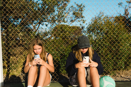 Close up of teenage girls with ball and on smart phones at netball court - Australian Stock Image