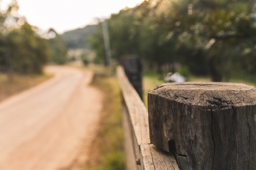 Close up of timber post of rural property fence, on side of winding dirt road - Australian Stock Image