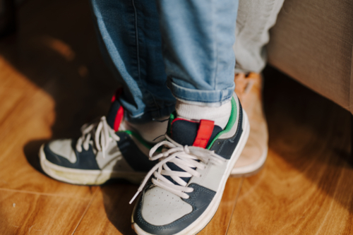 Close-up of two pairs of feet wearing sneakers resting against the wooden floor. - Australian Stock Image