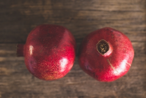 Close up of two red pomegranates with a wooden background