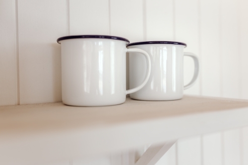 Close-up of two white mugs on shelf