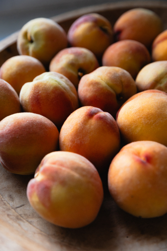 Close up of wooden bowl containing home grown ripe peaches in natural light - Australian Stock Image