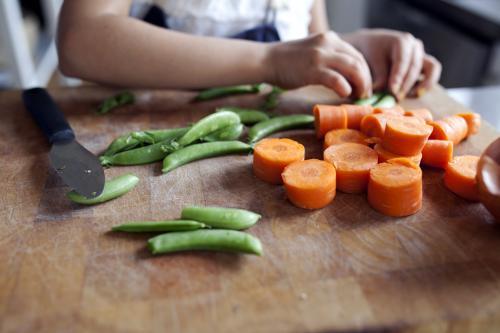 Close up of young child helping chop vegetables