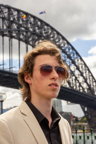Close up of young man dressed in suit standing with the Sydney Harbour Bridge in the background - Australian Stock Image