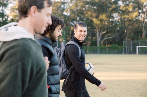 Close up photo of 3 young interracial men walking on the soccer field - Australian Stock Image