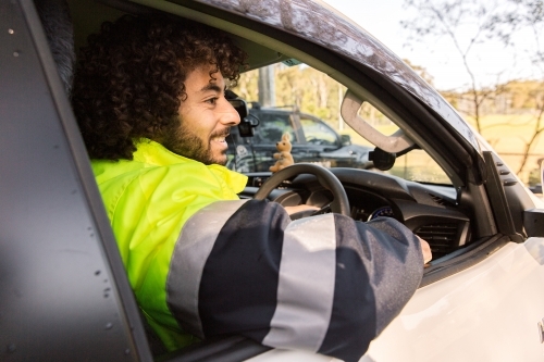 Close up photo of a man with curly hair wearing light green and grey jacket inside a black car - Australian Stock Image