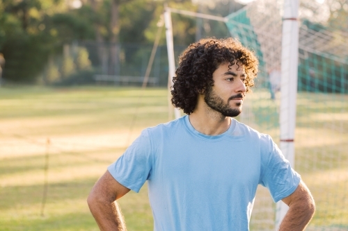 Close up photo of a man with curly hair with beard wearing blue shirt with arms against the hips - Australian Stock Image