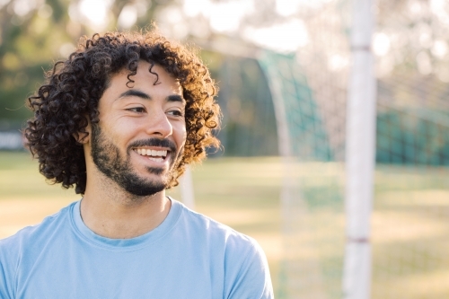 Close up photo of a smiling man with curly hair with beard wearing blue shirt on a sunny day
