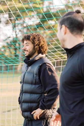 Close up photo of two interracial young men standing on the field near the net smiling - Australian Stock Image