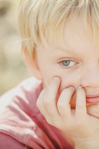 Close up portrait image of serious young blue eyed boy with chin resting on hand - Australian Stock Image