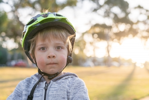 Close-up portrait of little boy wearing bicycle helmet at sunset - Australian Stock Image