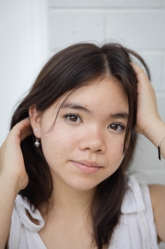 Close-up portrait of teenage girl with hands on her head - Australian Stock Image