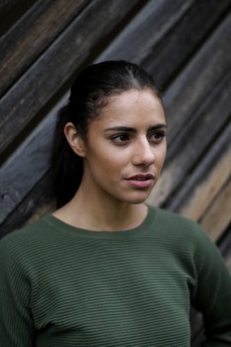 Close up portrait of young Fijian woman standing in front of textured wooden panels - Australian Stock Image