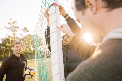 Close up shot of 3 interracial man on the field touching the soccer post and net with a soccer ball - Australian Stock Image