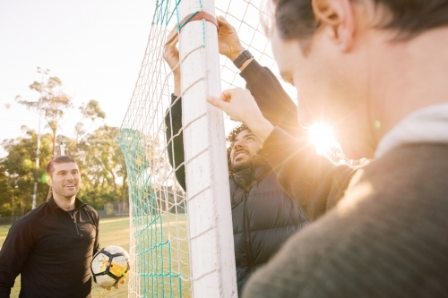 Close up shot of 3 interracial man on the field touching the soccer post and net with a soccer ball