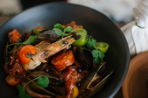 Close up shot of a bowl of large prawns with mussels topped with green leaves and tomatoes - Australian Stock Image