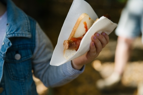 Close up shot of a person holding a sausage sandwich with ketchup in a sandwich tissue