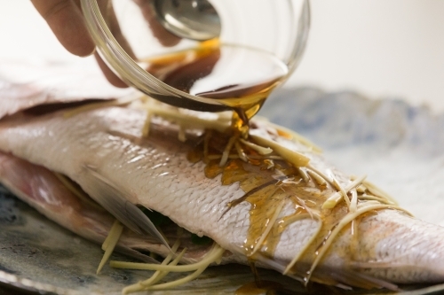 Close up shot of a raw white fish sliced in half  topped with thinly sliced ginger and soy sauce - Australian Stock Image