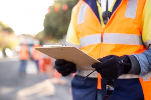 Close up shot of a road worker wearing orange and yellow jacket holding his notes