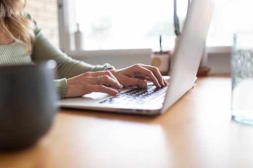 close up shot of a woman's hand on the laptop keyboard on a wooden table