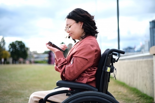 close up shot of a woman with disability sitting in a wheelchair while looking at her mobile phone