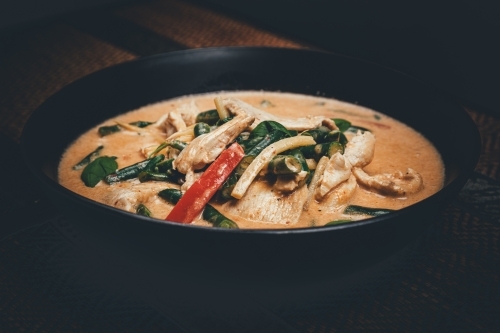 Close up shot of red curry chicken in a black bowl - Australian Stock Image