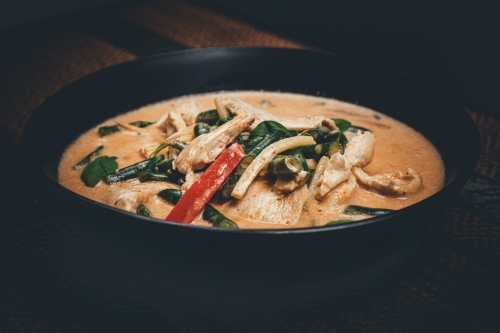 Close up shot of red curry chicken in a black bowl