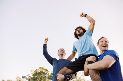 close up shot of two men carrying a man on their shoulders while raising their arms up high