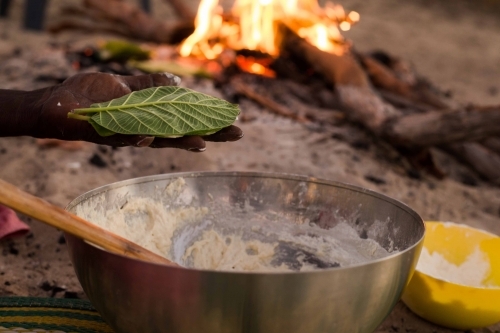 Close up shot of woman holding a leaf with a big bowl of flour on the ground and a flame on the back - Australian Stock Image