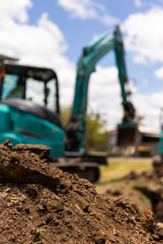 Close-up view of freshly dug soil in the foreground with a teal excavator in the background - Australian Stock Image