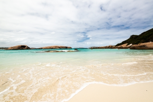 Close up view of water's edge at a cove with swimmer in the distance and islands - Australian Stock Image