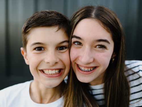 Closeup of brother and sister smiling at the camera. - Australian Stock Image