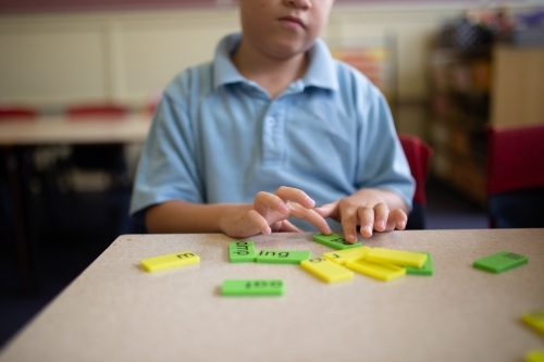 Closeup of primary school student's fingers on word tiles sitting at a desk