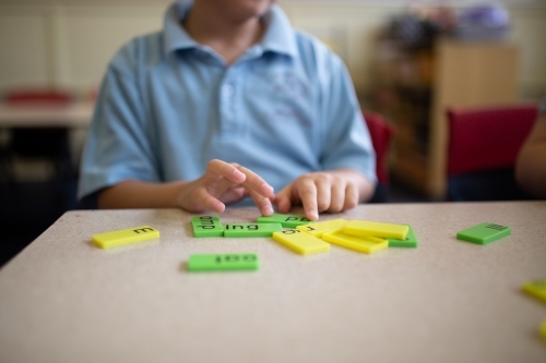 Closeup of primary school student's hands working with green and yellow word tiles - Australian Stock Image