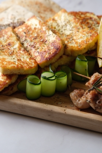 Closeup of seared halloumi cheese with thin slices of cucumber rolled up served on a wooden board - Australian Stock Image