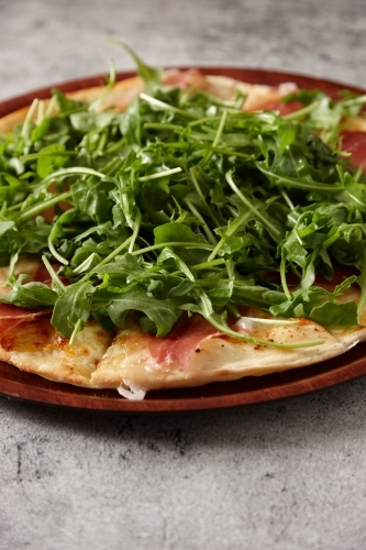 Closeup of Prosciutto Arugula pizza on a wooden board - Australian Stock Image