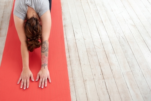 closeup woman in child's pose on red yoga mat in studio