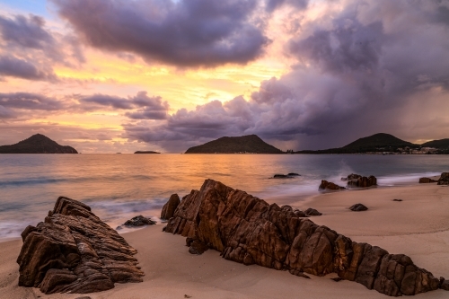 Cloudy sunrise over mountains and rocky beach - Australian Stock Image