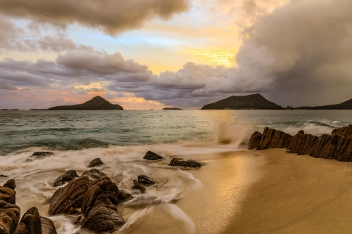 Cloudy sunrise over mountains and rocky beach - Australian Stock Image