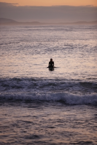 Surfer waiting on ocean on sunrise - Australian Stock Image