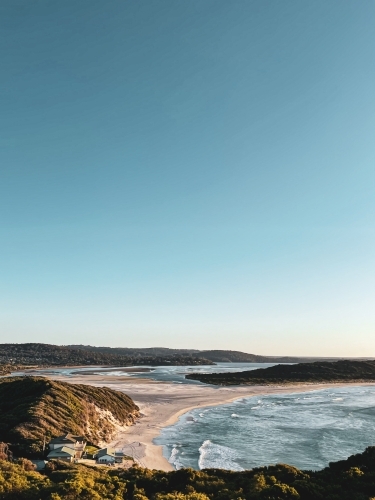 Coastal long shot of bay meeting river mouth with surf club buildings on beach