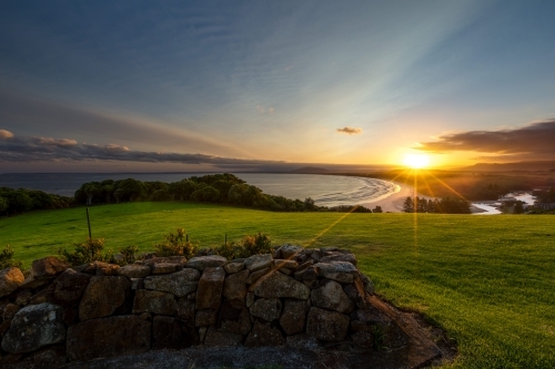 Coastal sunset landscape with rock wall, lush grass and beach - Australian Stock Image