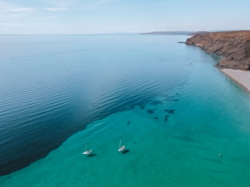 Coastline with rolling hills and boats and two tones coloured blue ocean from above - Australian Stock Image